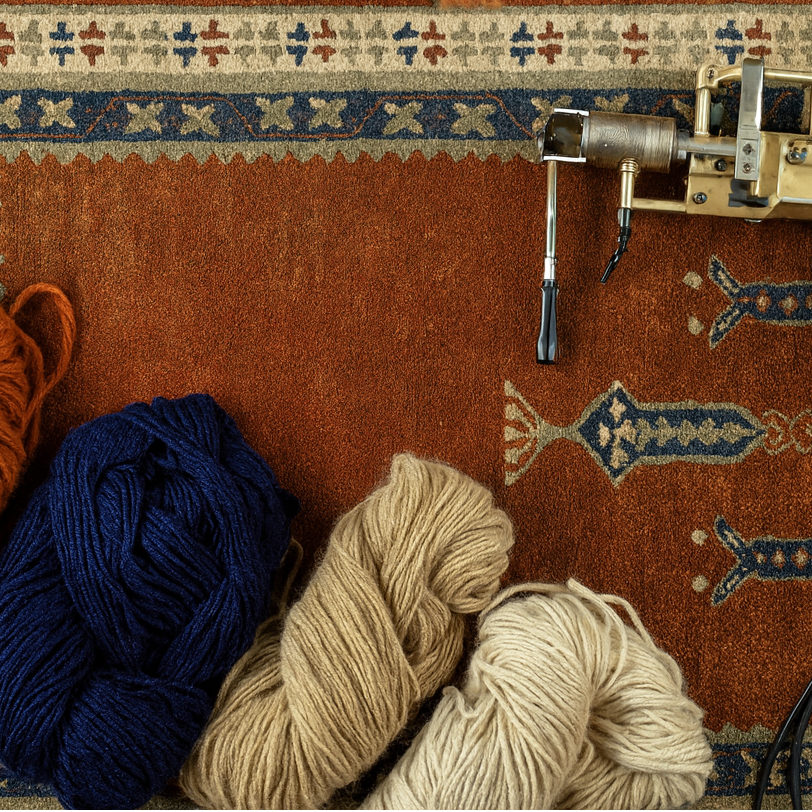 Yarn balls and a knitting machine on a patterned rug with scissors.